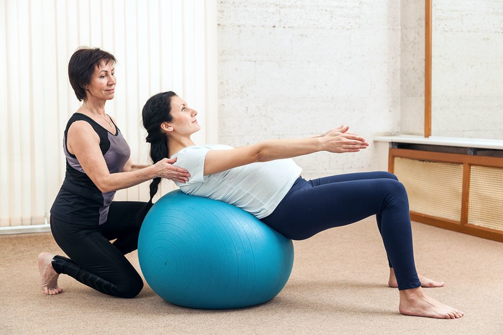 Gestante em sessão de fisioterapia fazendo exercício na bola de pilates