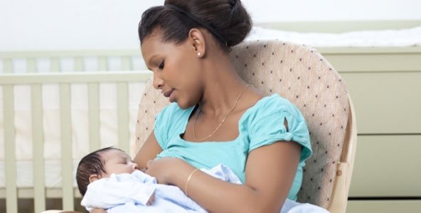 Mãe afro descendente sentada numa poltrona e amamentando seu bebê