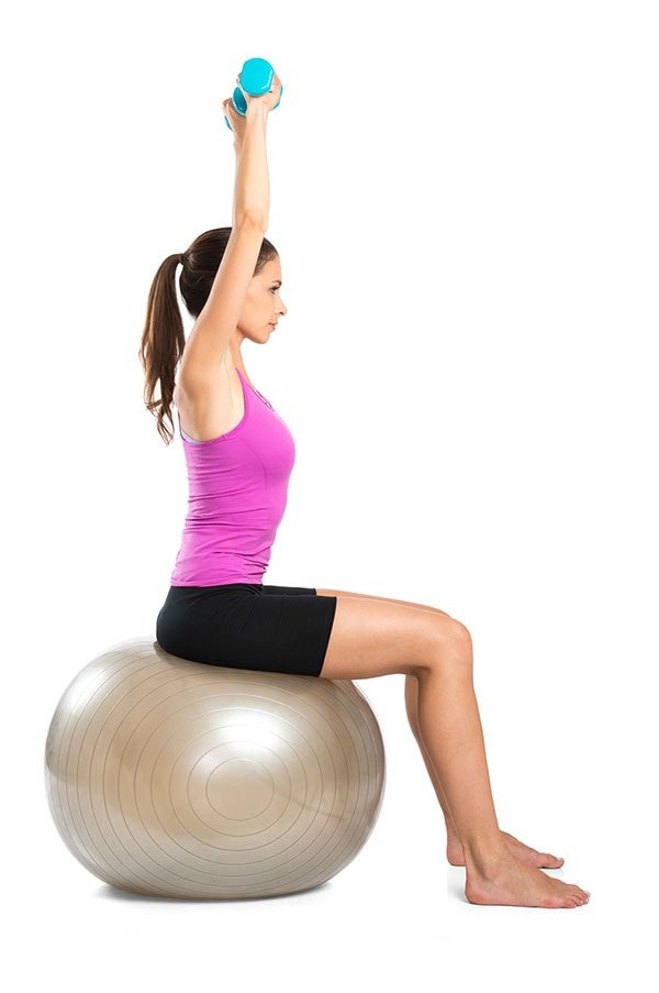 Mulher se alonga com pesos nas mãos sobre uma bola de pilates